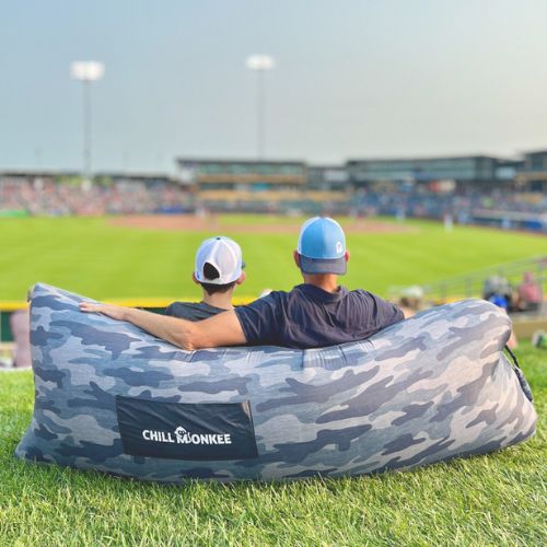 Father and son sitting in a gray camo patterned Chill Monkee inflatable lounger at a baseball game