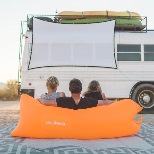 Father with two children sitting in an orange Chill Monkee inflatable lounger watching an outdoor movie
