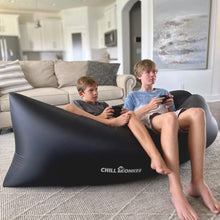 Load image into Gallery viewer, Two young boys sitting in a black Chill Monkee inflatable lounger playing a video game
