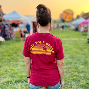 Rear view of a woman wearing the Chill Your Monkee Sunset Graphic Tee at a hot air balloon festival