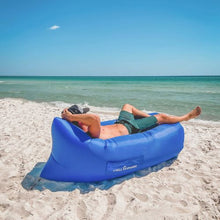 Load image into Gallery viewer, Man laying in a dark blue Chill Monkee inflatable lounger on the beach
