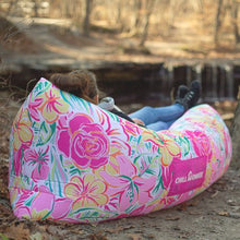 Load image into Gallery viewer, Hiker resting in a floral patterned Chill Monkee inflatable lounger next to a waterfall
