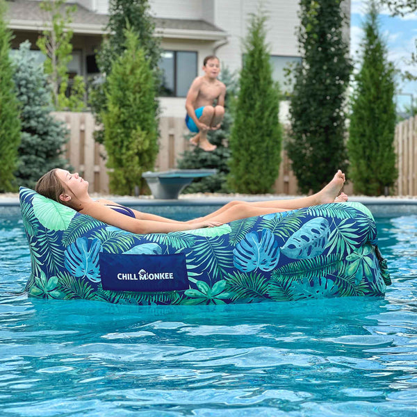 Young woman floating in a pool on a tropical-patterned Chill Monkee inflatable lounger