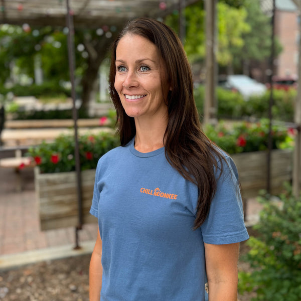 Front view of a woman wearing the Life Relaxed Beach Hammock Graphic Tee outside a local cafe