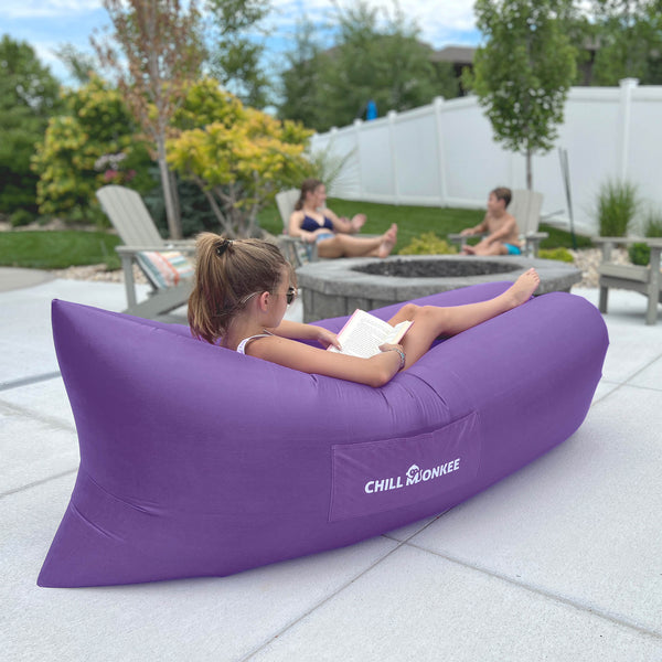 Young girl reading a book in a dark purple Chill Monkee inflatable lounger