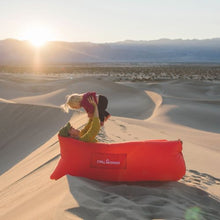 Load image into Gallery viewer, Mother laying in a red Chill Monkee inflatable lounger with her daughter in the desert

