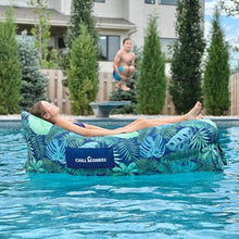 Load image into Gallery viewer, Young girl floating in a pool in a tropical patterned Chill Monkee inflatable lounger
