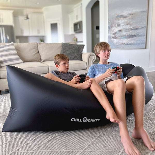 Two boys playing a video game on a Chill Monkee Black Lazy Lounger in a living room.