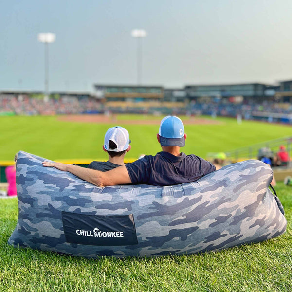 Father and son relaxing on a Chill Monkee Gray Camo Lazy Lounger at a baseball stadium.