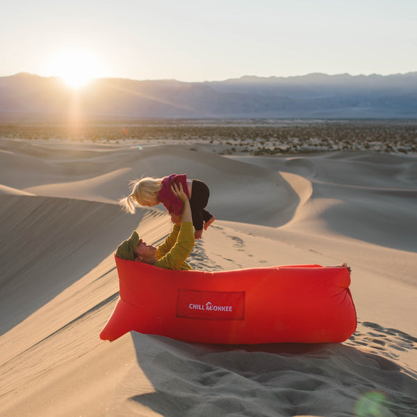 Mother and child lounging on a Chill Monkee Red Lazy Lounger on sand dunes.