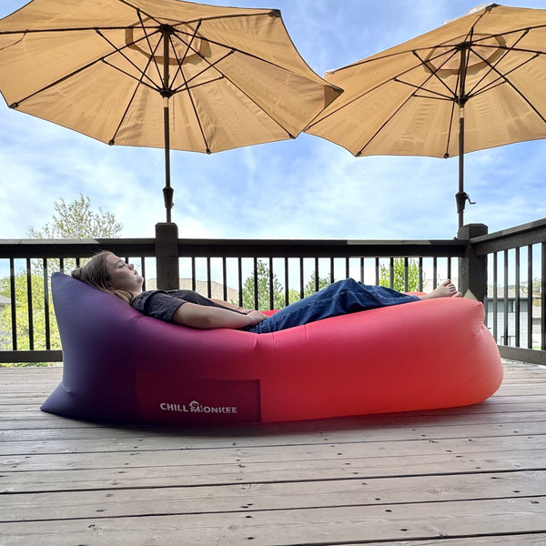 Chill Monkee Sunset Fade inflatable lazy lounger on a deck under patio umbrellas.